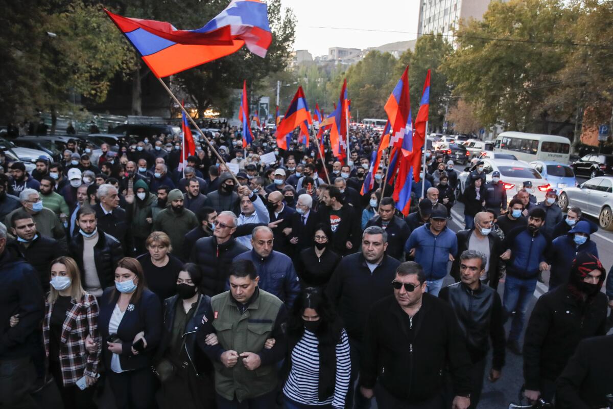 Protesters, a few in masks and some holding Armenian flags, crowd together and lock arms. 