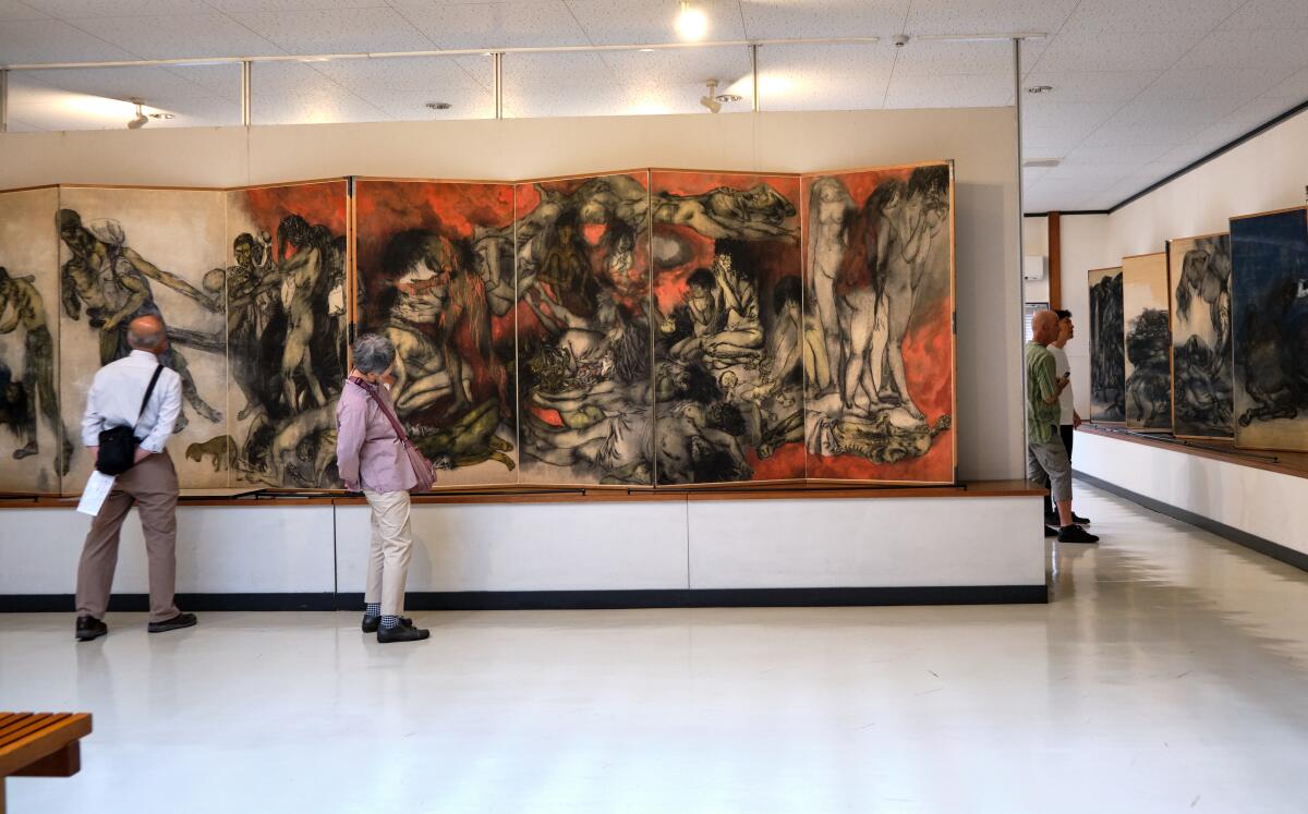 Visitors gaze at large-scale rice paper paintings that show bodies surrounded by flame