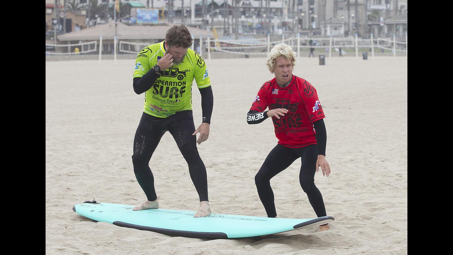 Air Force veteran Eric Stoneking, left, follows surf instructor Tanner Hendrickson, who shows him how to get to his feet during opening day of Operation Surf in Huntington Beach on Wednesday.