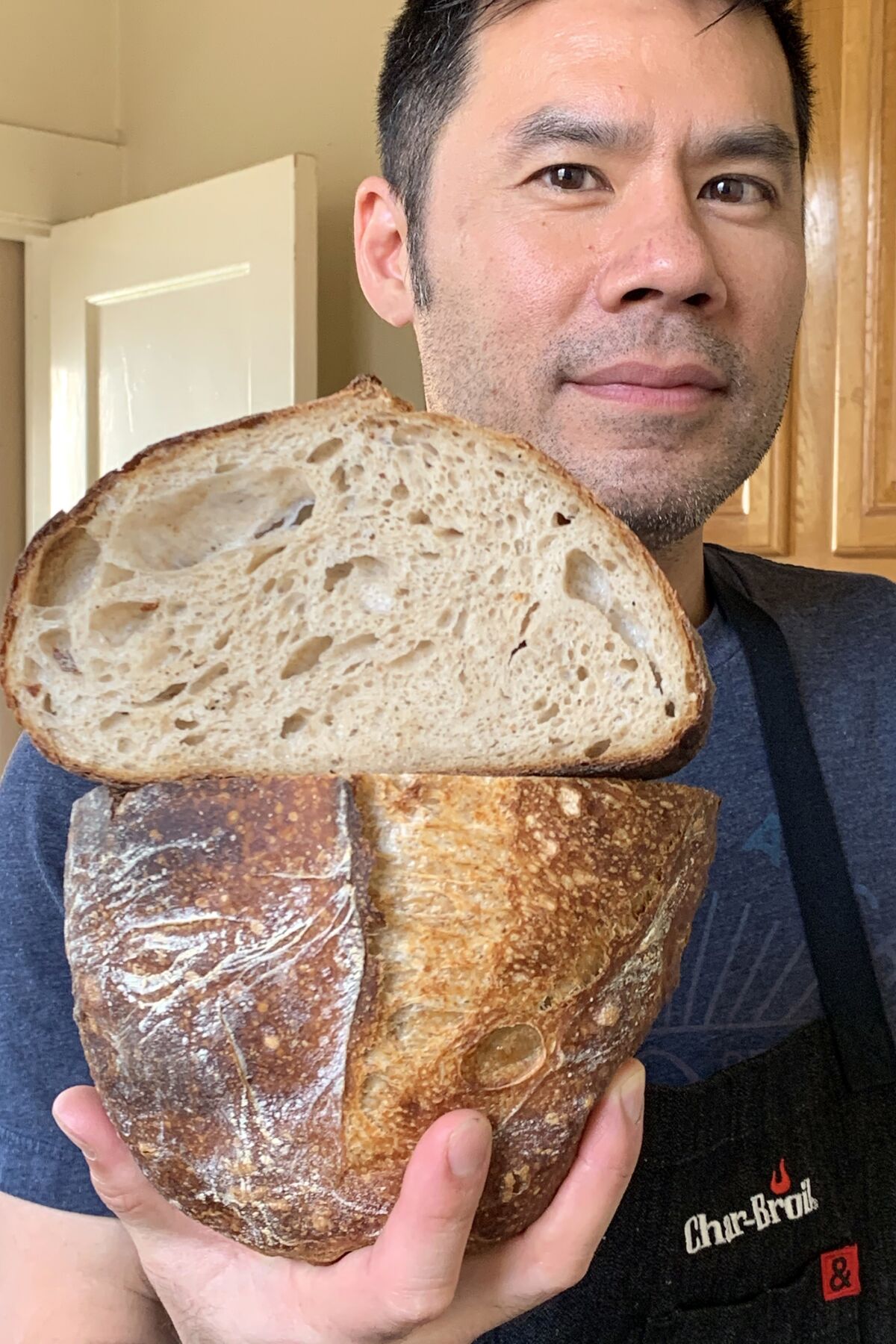 A man holds up a loaf of his sourdough bread, with the top portion sliced open to show the interior texture.