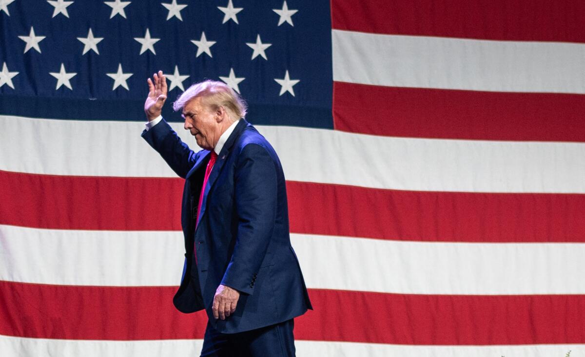 Former President Trump lifts a hand as he walks in front of a U.S. flag