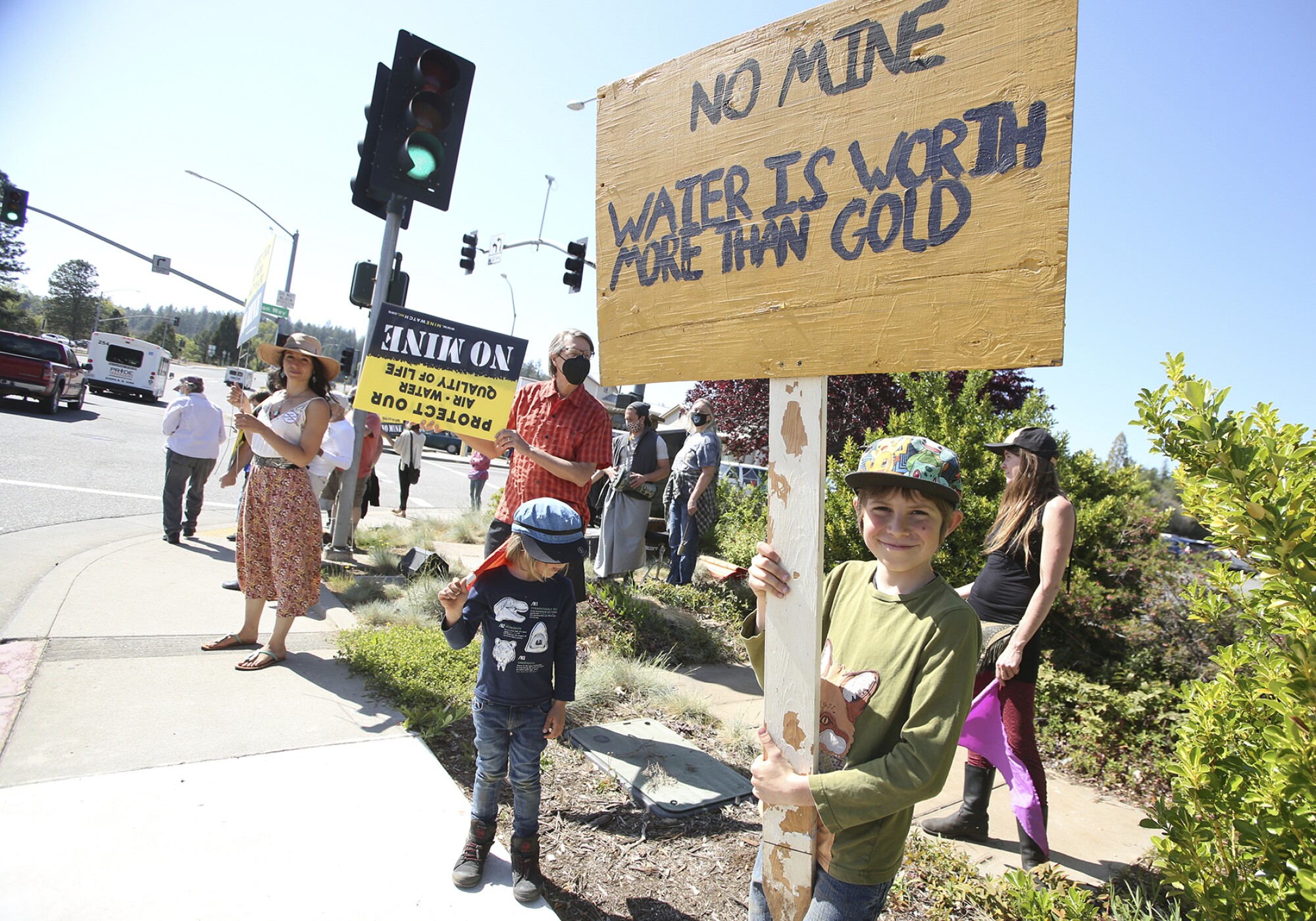 Children and others hold signs at a street corner protest. 