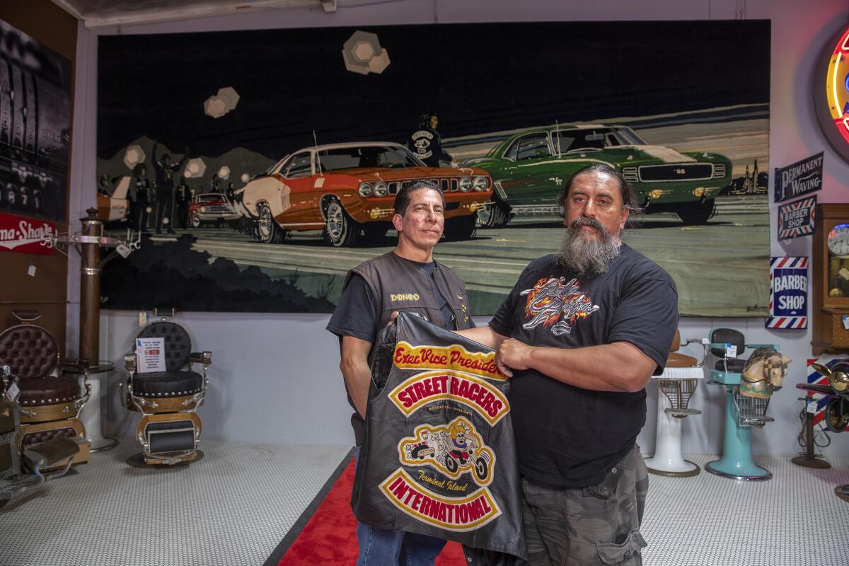 Donald Galaz, left, and Fabian Arroyo, members of the Brotherhood of Street Racers, pose in front of a tapestry commissioned by former Los Angeles Times Publisher Otis Chandler.