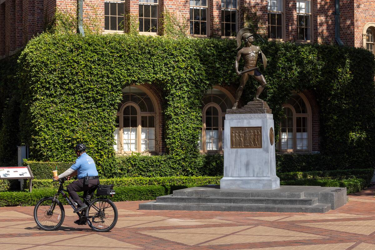 A security officer on a bike patrol rolls past Tommy Trojan statue.