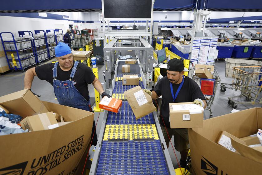 San Diego, CA, November 30, 2023: Distribution clerks Ross Albers, left, and Piero Cavallini put packages on a new Automated Delivery Unit Sorter (ADUS), which is used to automate sorting of smaller packages at Chula Vista's Main Post Office on Thursday, November 30, 2023. The location has been selected as a new sorting and delivery center for Chula Vista and Imperial Beach. (K.C. Alfred / The San Diego Union-Tribune)