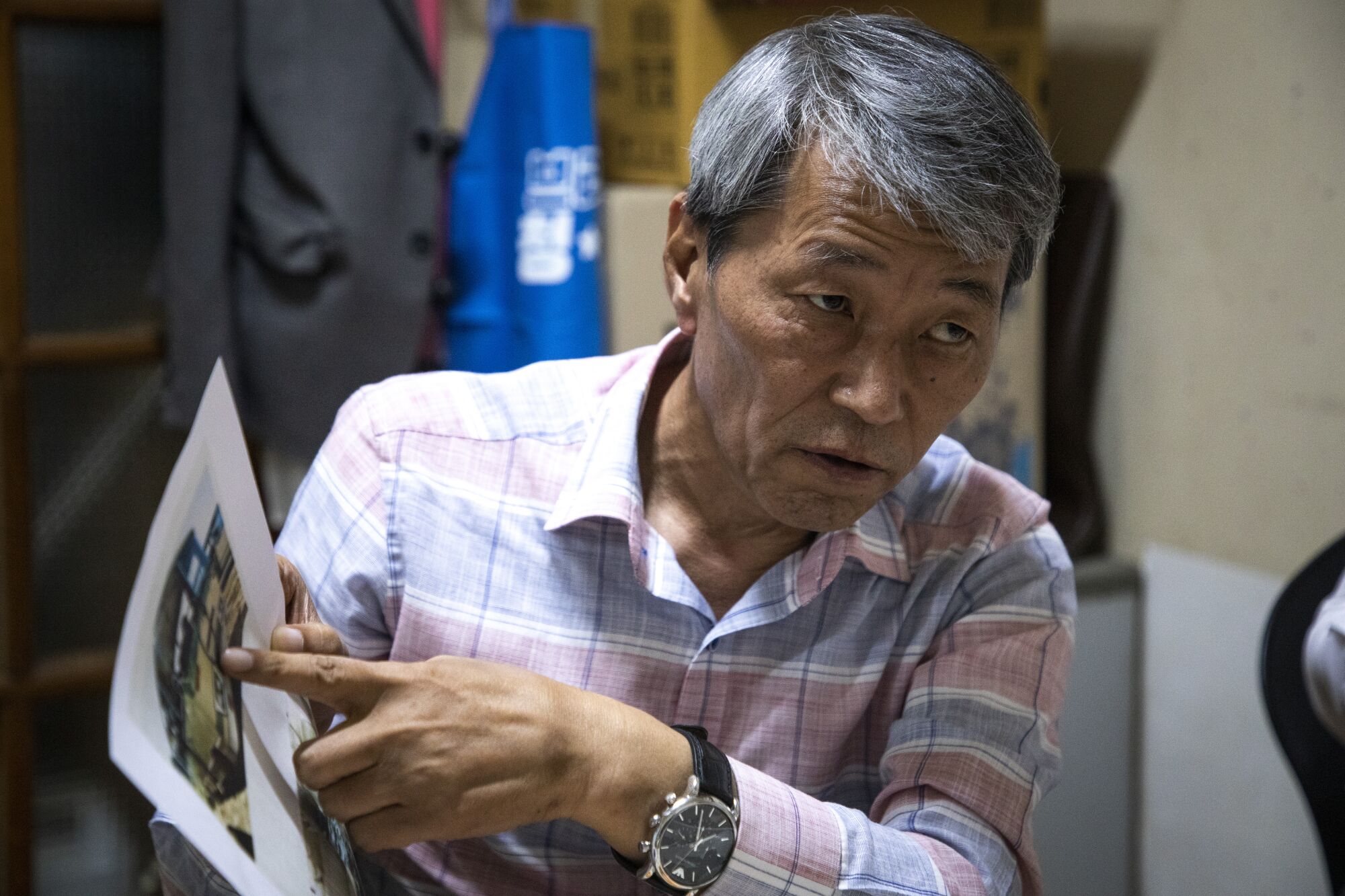 A gray-haired man points to an image on a piece of paper he is holding while looking intently at someone he is talking to.