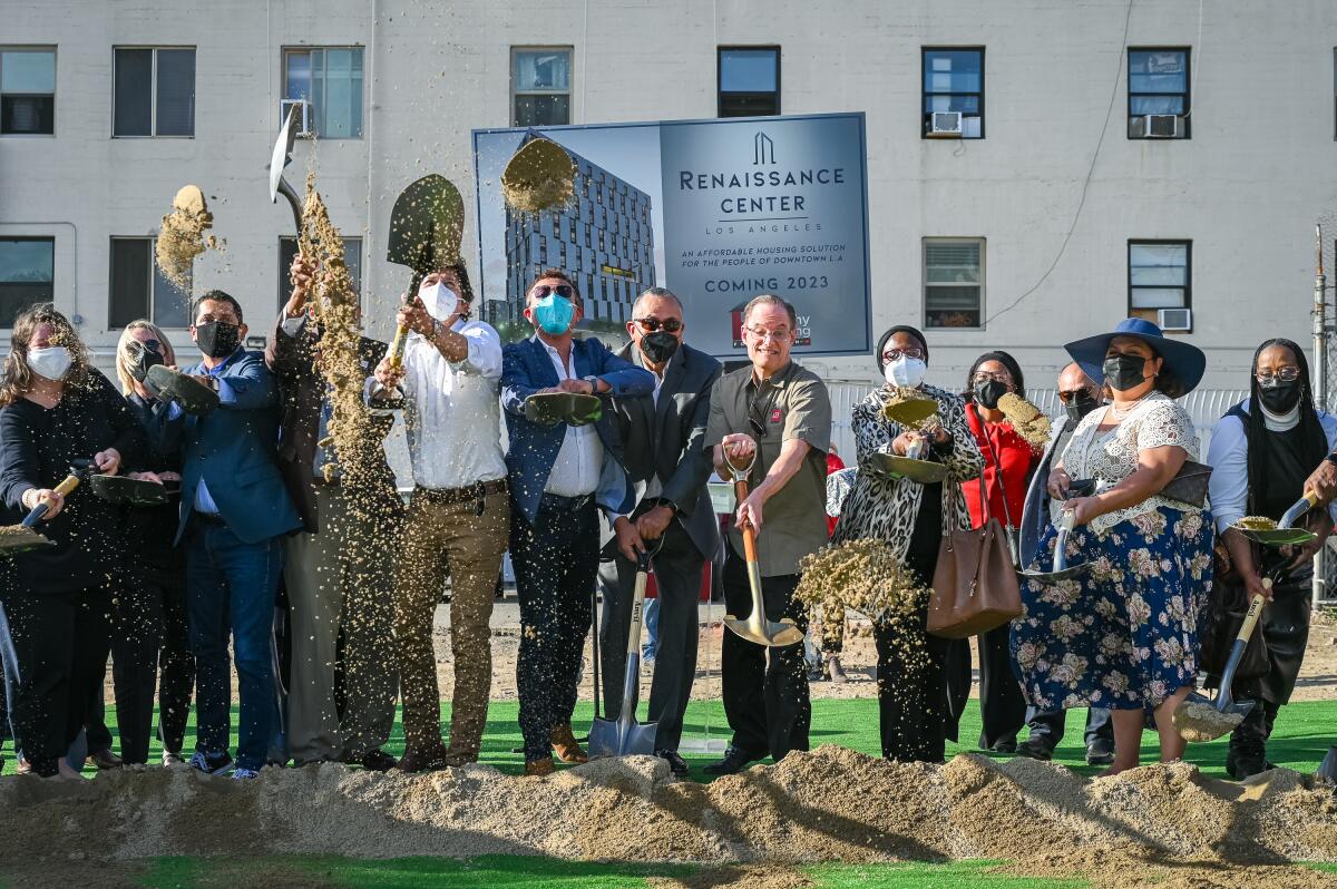 People, some wearing protective masks, hold shovels with dirt next to a sign that says "Renaissance Center"