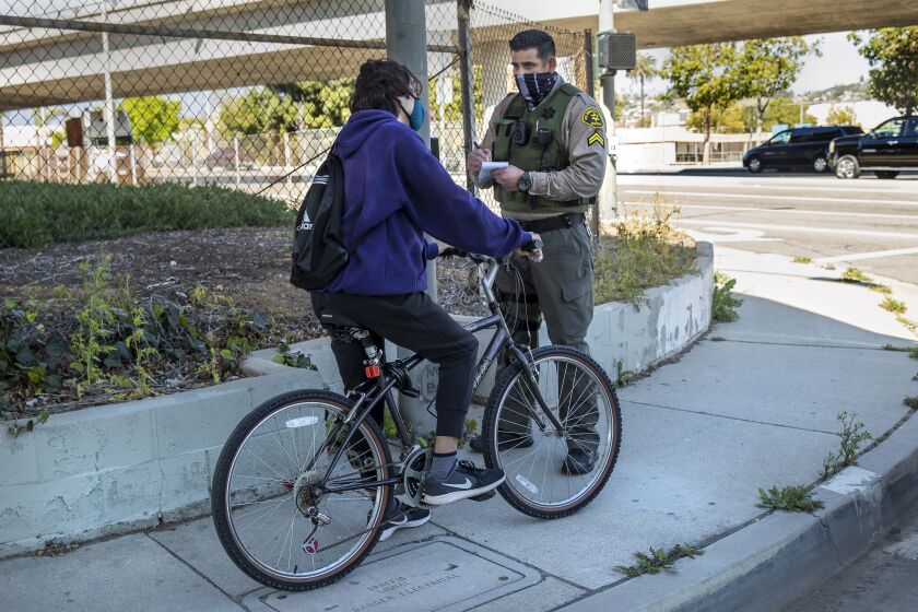 EAST LOS ANGELES, CA - MARCH 24, 2021: L.A. County Sheriff's Deputy Manan Butt gives a warning to a bicyclist for riding on the sidewalk and going in the wrong direction on 1st St. near Ford Blvd. in East Los Angeles. (Mel Melcon / Los Angeles Times)