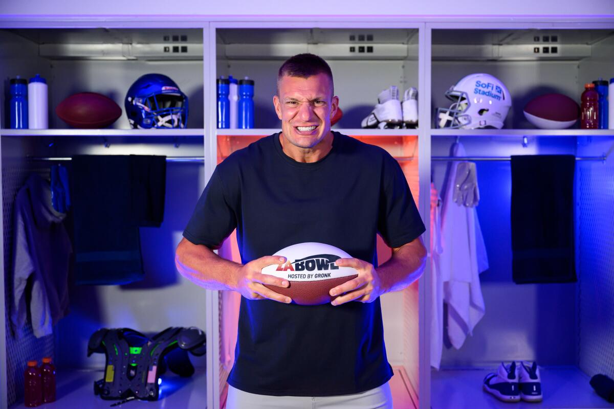 Rob Gronkowski stands in front of lockers holding a football at SoFi Stadium.