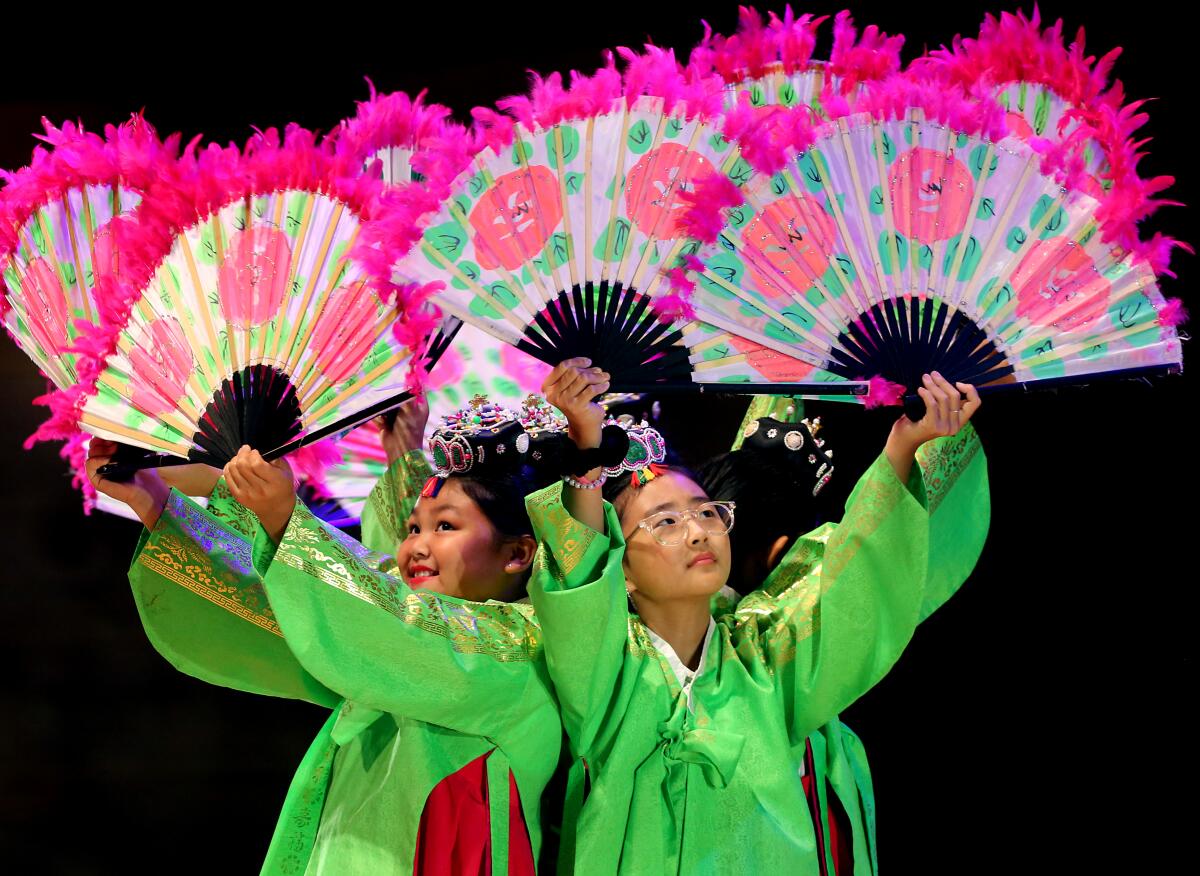 Young students in green tunics hold up colorful fans during a fan dance.