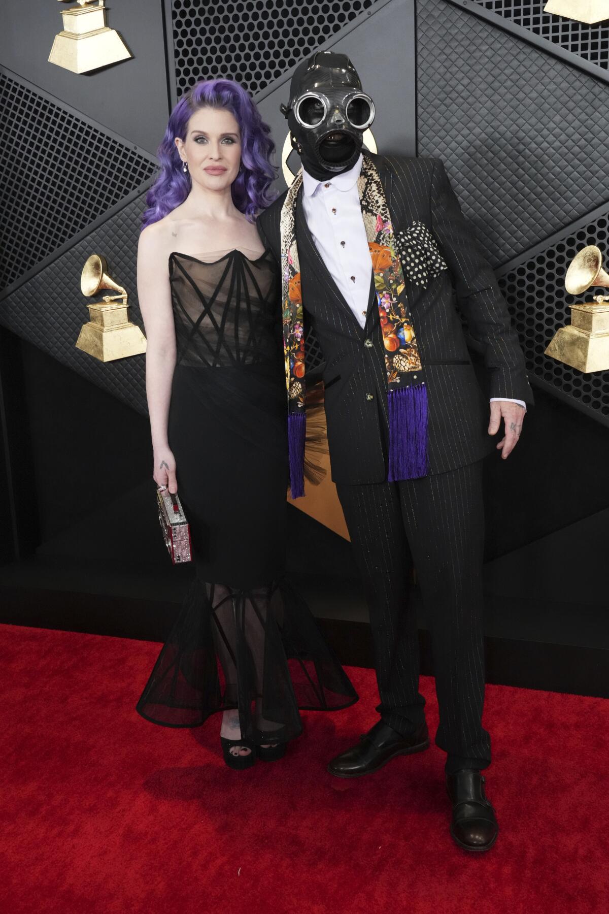 Kelly Osbourne standing in a black gown and purple hair with Sid Wilson clad in formal attire and a mask with large goggles