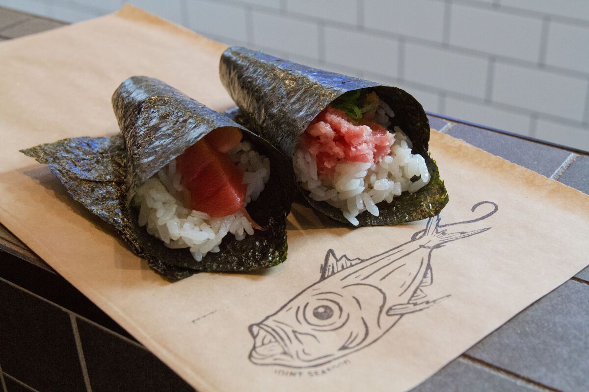 A photo of two hand rolls, lean tuna and fatty tuna, on the counter atop brown paper featuring a line drawing of a fish