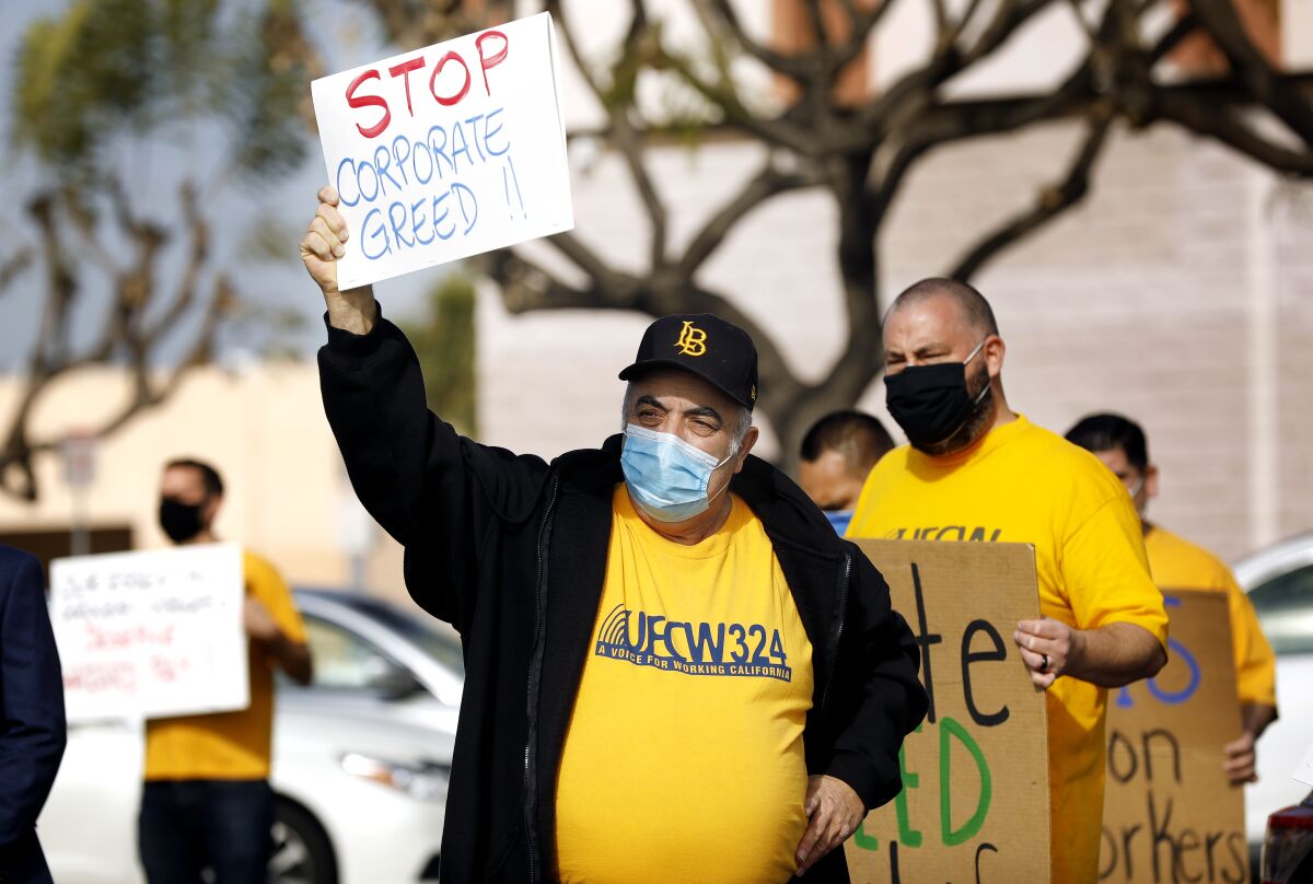 A man holds a sign that says, "Stop Corporate Greed' during a protest at a grocery store.