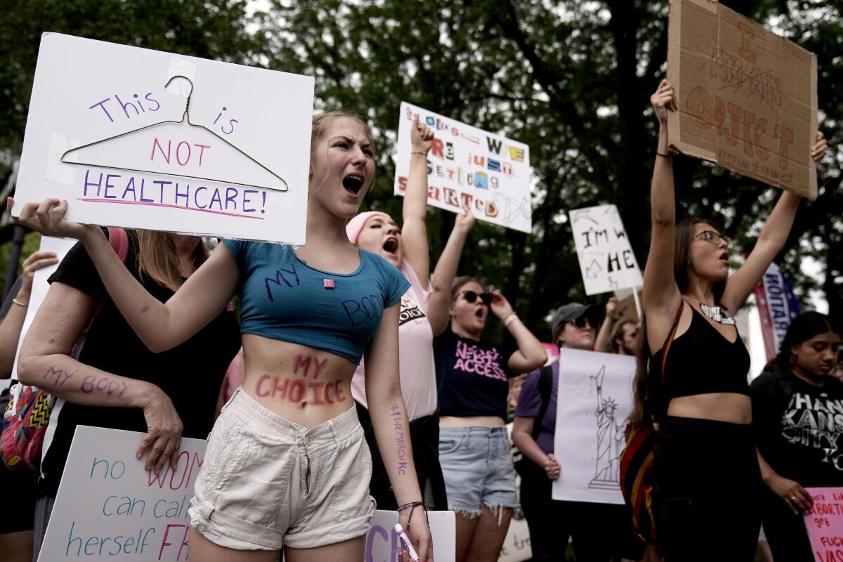 Women hold up signs, including one showing a coat hanger and the words "This is not healthcare"