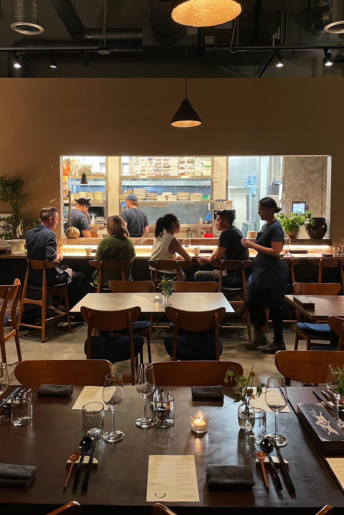 A vertical photo of guests seated at the chef's counter, kitchen visible beyond them.