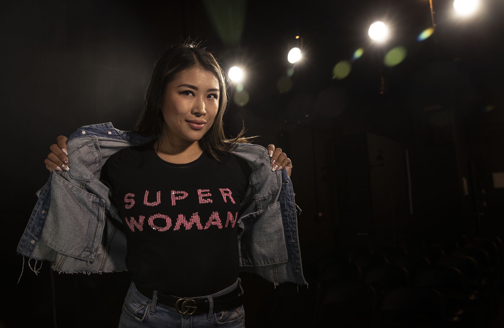 A woman holds open a jean jacket showing herself wearing a t-shirt reading "super woman"