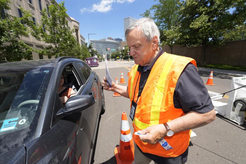 Election judge Adam Ballinger accepts a ballot from a motorist passing through a drive-up polling location outside the Denver Elections Division headquarters Tuesday, June 28, 2022, in Denver. (AP Photo/David Zalubowski)