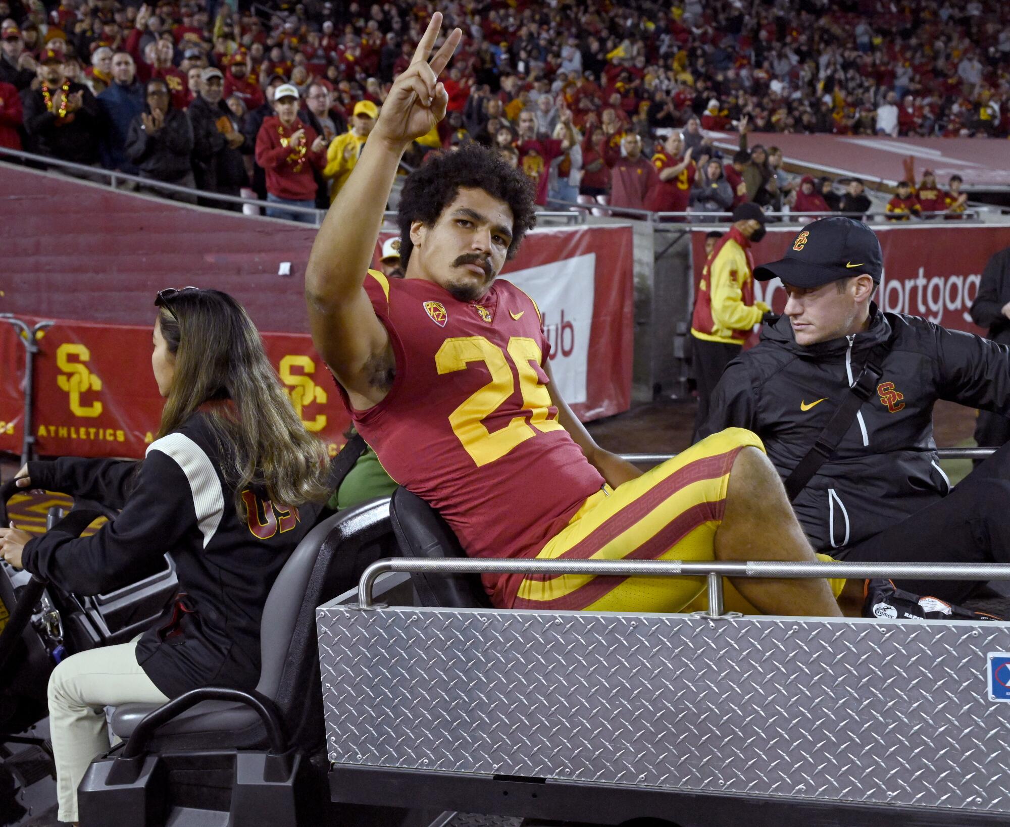 USC running back Travis Dye waves to the crowd while being taken off the field on a cart Friday at the Coliseum.