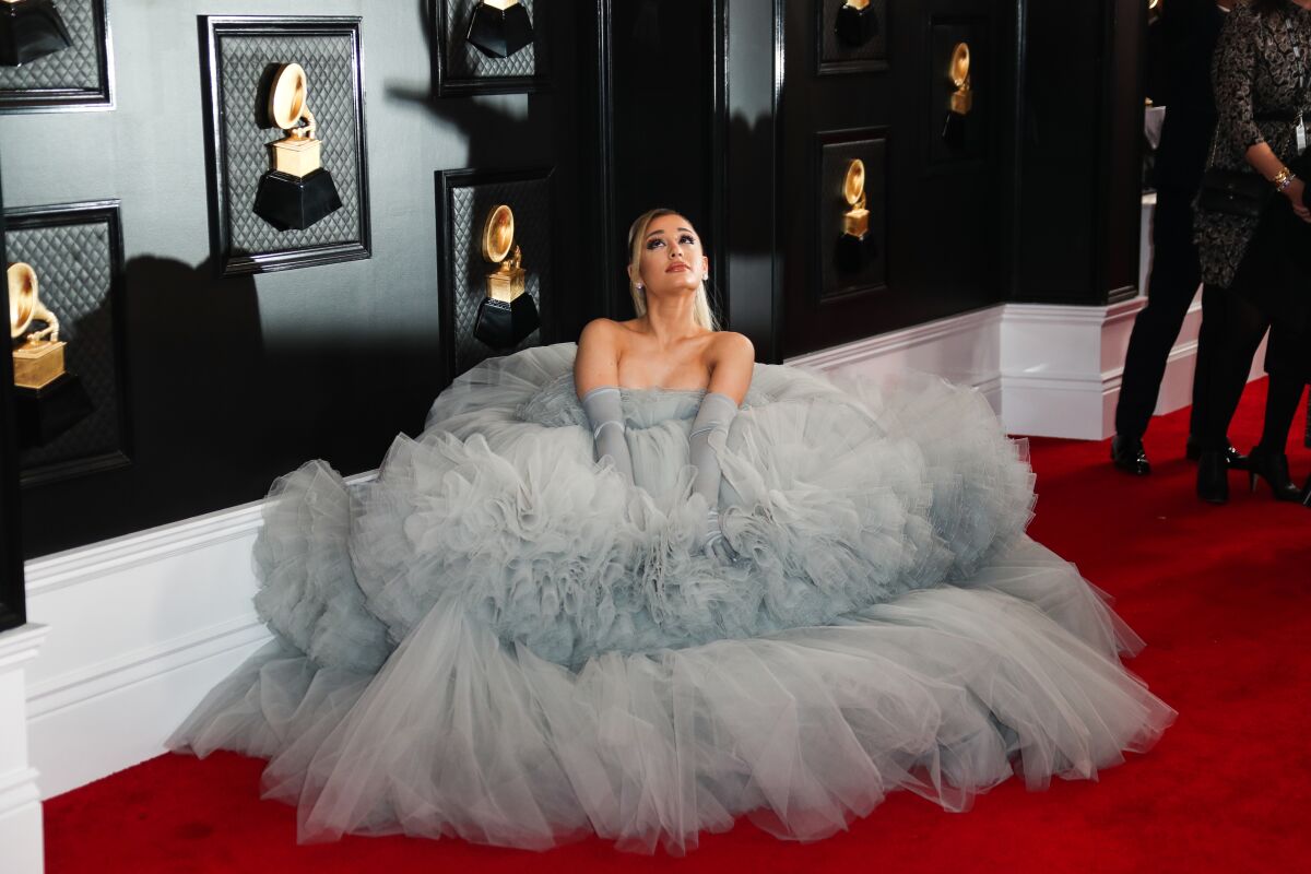 Ariana Grande sits on a red carpet surrounded by her fluffy gray gown