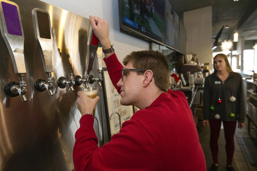 ENGLEWOOD, CO-DECEMBER 13, 2019: Alex Randall, 29, a bartender at Brewability in Englewood, Colorado, who is legally blind, pours a beer from the tap as Chelsea Whitaker, a manager and occupational therapist looks on. (Mel Melcon/Los Angeles Times)