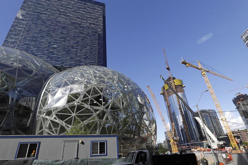 FILE - In this Wednesday, Oct. 11, 2017, file photo, large spheres take shape in front of an existing Amazon building, behind, as new construction continues across the street in Seattle. Amazon said Wednesday, May 2, 2018, it is pausing construction on a new high-rise building in Seattle while it awaits the outcome of a city proposal to tax worker hours. The Seattle City Council has been weighing a proposed "head tax" on high-grossing businesses as a way to raise about $75 million a year for affordable housing and homelessness services. (AP Photo/Elaine Thompson, File)