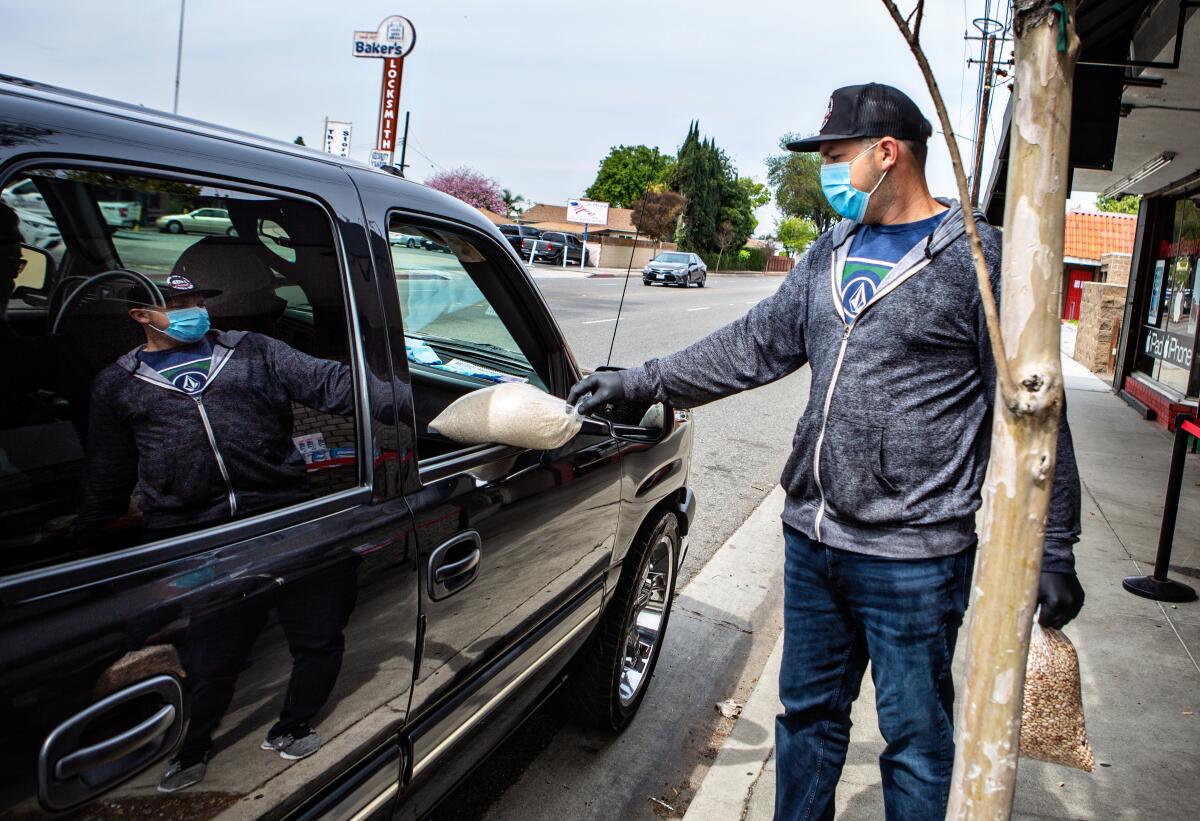 David Fuerte of Masataco in Whittier delivers bags of rice and beans to a customer during the coronavirus pandemic on March 31. Fuerte converted his vegan Mexican restaurant into a curbside, drive-up operation and recently adding medical-grade face masks to the menu.