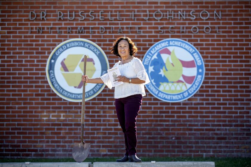 Janice Munemitsu, the author of "The Kindness of Color," poses for a photo in front of Johnson Middle School in Westminster on Tuesday, October 19. Munemitsu is holding a shovel from the family farm that used to sit on the site of the school.