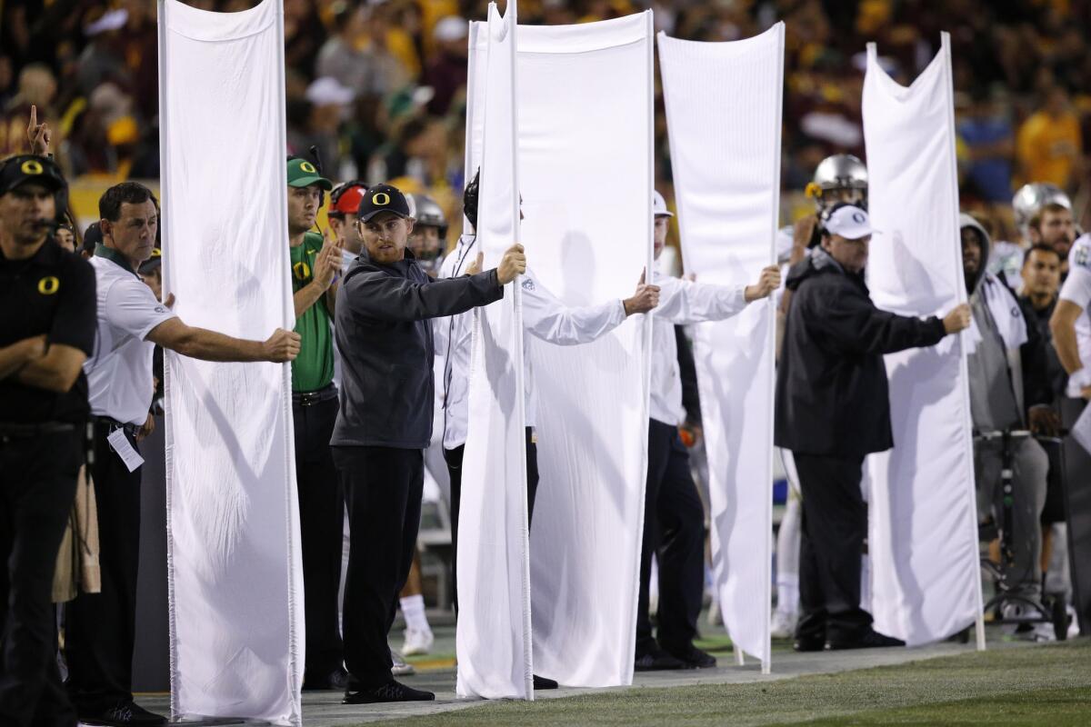 Oregon sideline personnel hold up sheets to shield play call signals during the Ducks' triple-overtime victory over Arizona State, 61-55, Thursday night.