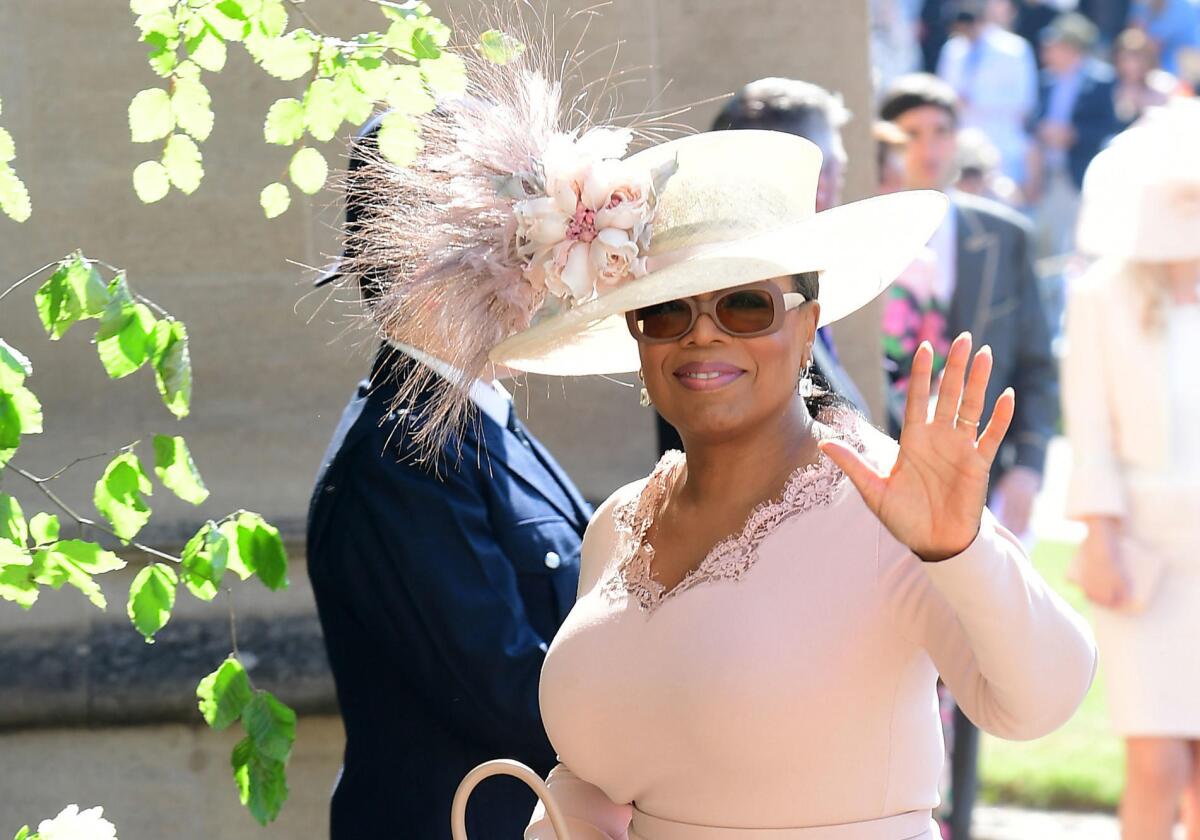 Oprah Winfrey, wearing a hat, waves