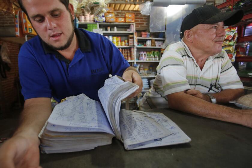 Lorenzo Gastelum, izquierda, y su papa, Israel, trabajan en la caja de la tienda de la compañía en el Campo Isabeles, cerca de Culiacán, Sinaloa.