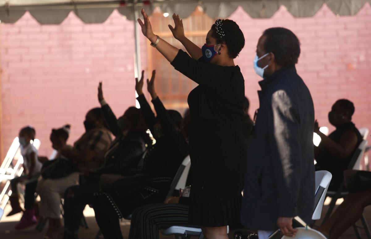 Outside a church, folding chairs are set up for parishioners, who lift their arms as they listen to a sermon.