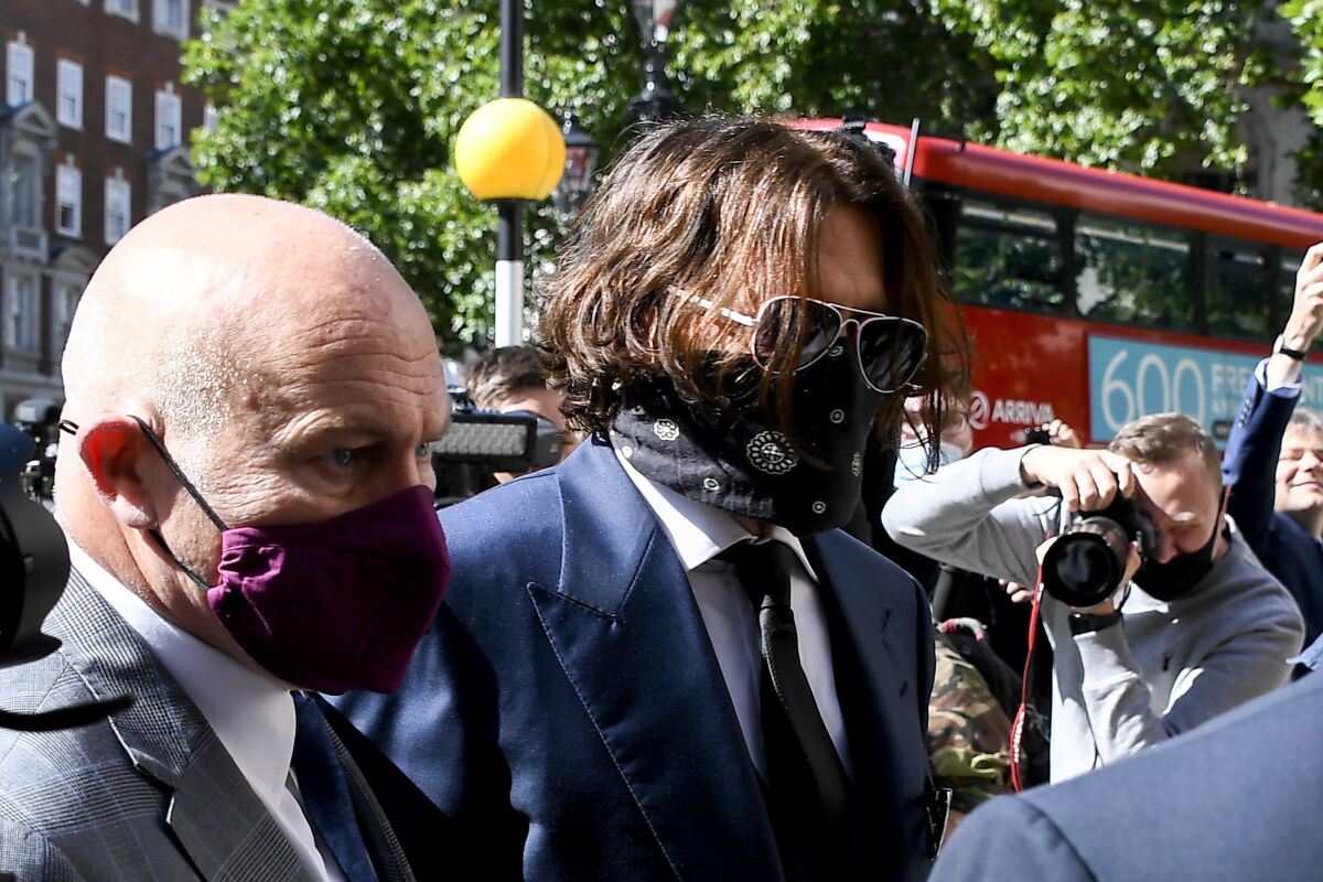 Johnny Depp wears sunglasses and a face covering as he walks through a crowd.