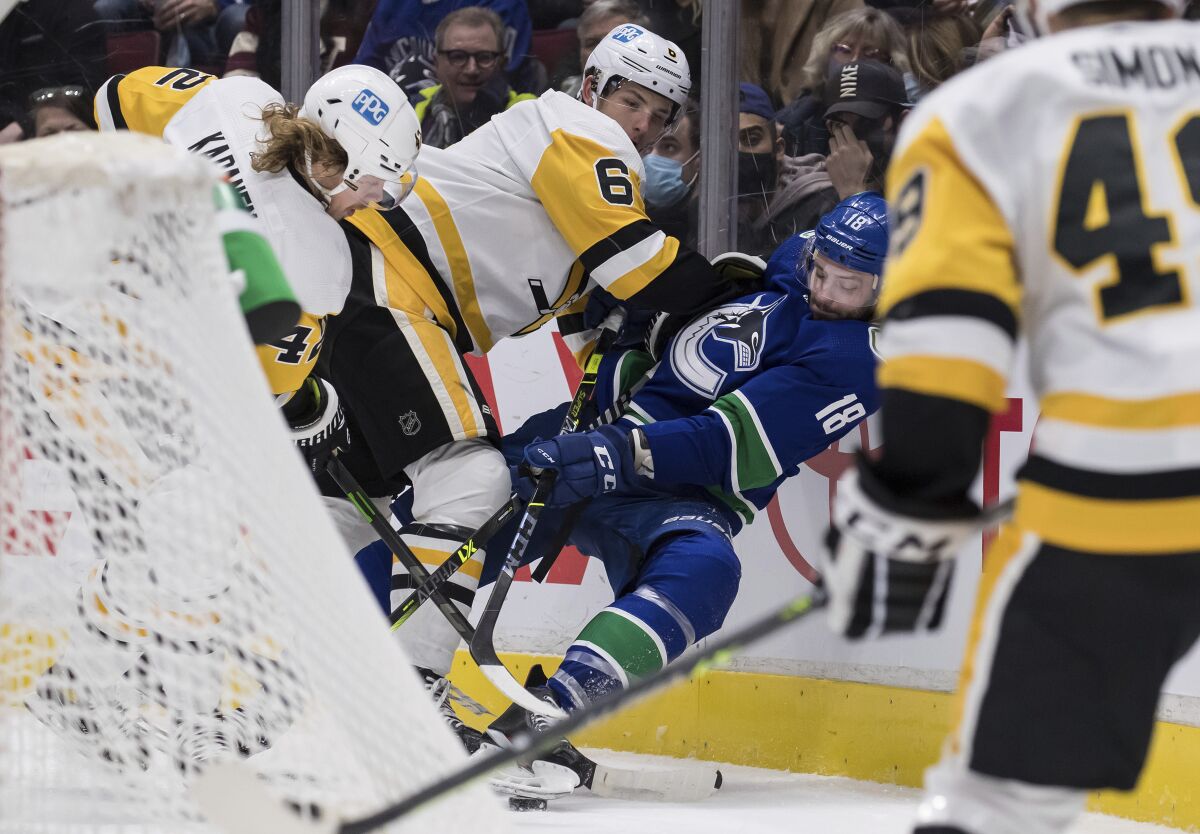 Pittsburgh Penguins' John Marino (6) checks Vancouver Canucks' Jason Dickinson (18) during the second period of an NHL hockey game Saturday, Dec. 4, 2021, in Vancouver, British Columbia. (Darryl Dyck/The Canadian Press via AP)