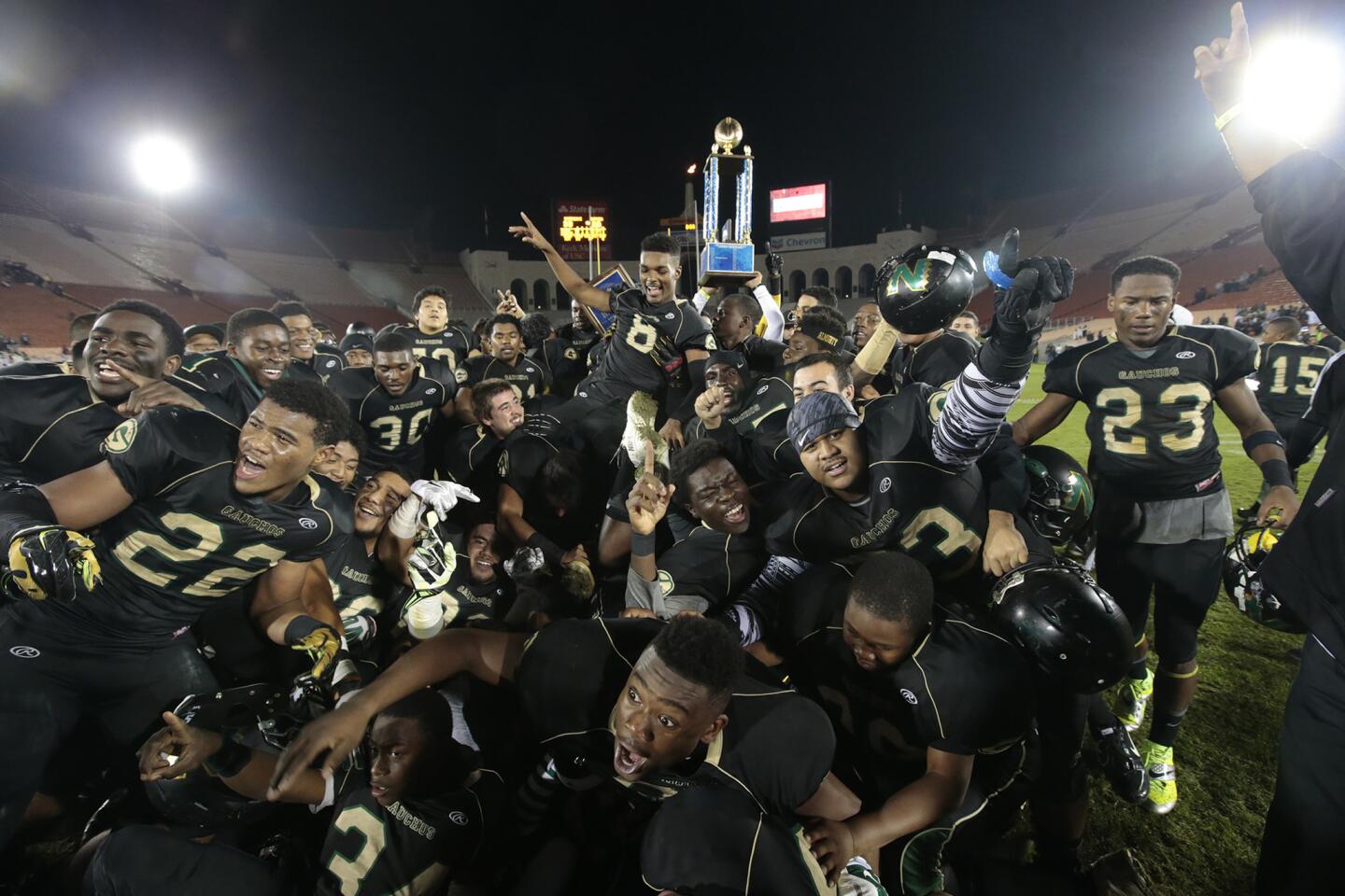 Narbonne players pile onto each other as they take a team picture following their 33-20 victory over Carson in the City Seciton Division I championship game on Saturday night at the Coliseum.