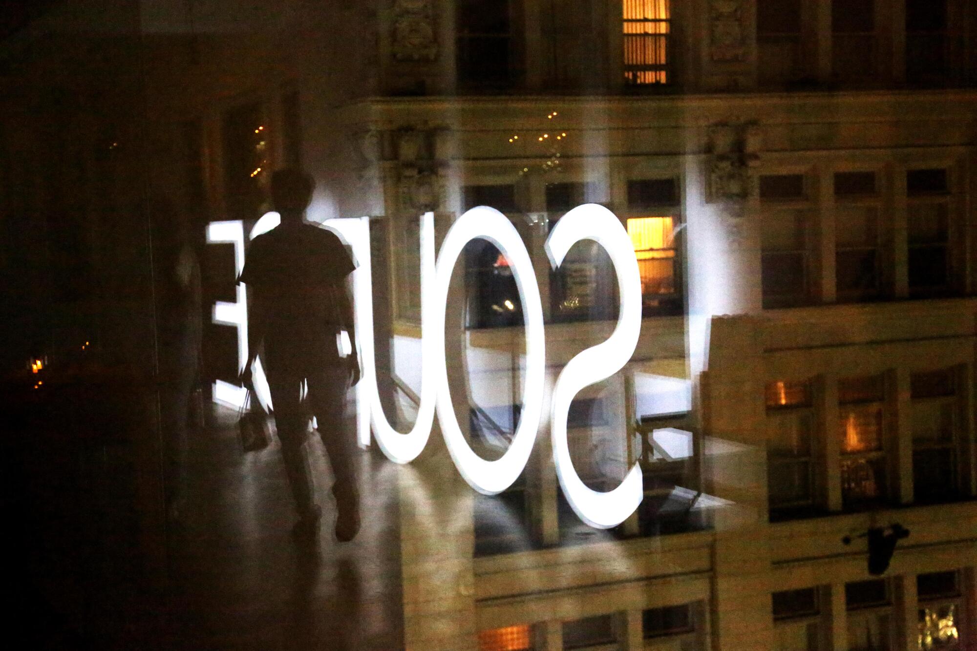 The silhouette of a person  in a dark room against the reflection of the word Source in large, white letters