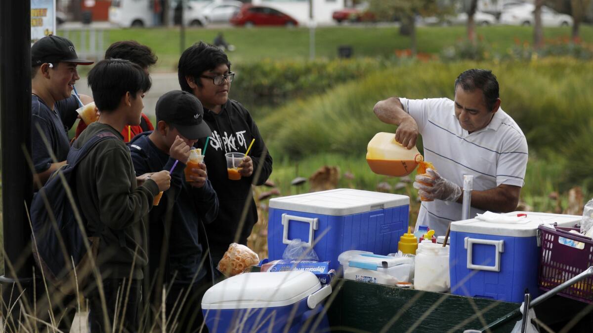 Street vendor Neftali Lopez serves customers from his food cart in Echo Park in Los Angeles. The Huntington Beach City Council on Monday approved a permanent permit process for sidewalk vendors, with strict limits.