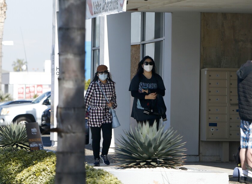 Women wearing masks walk past business.