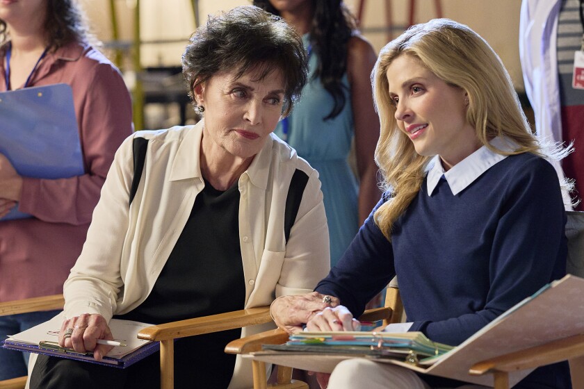 Two women seated, one with a notepad, one looking through a binder of material.