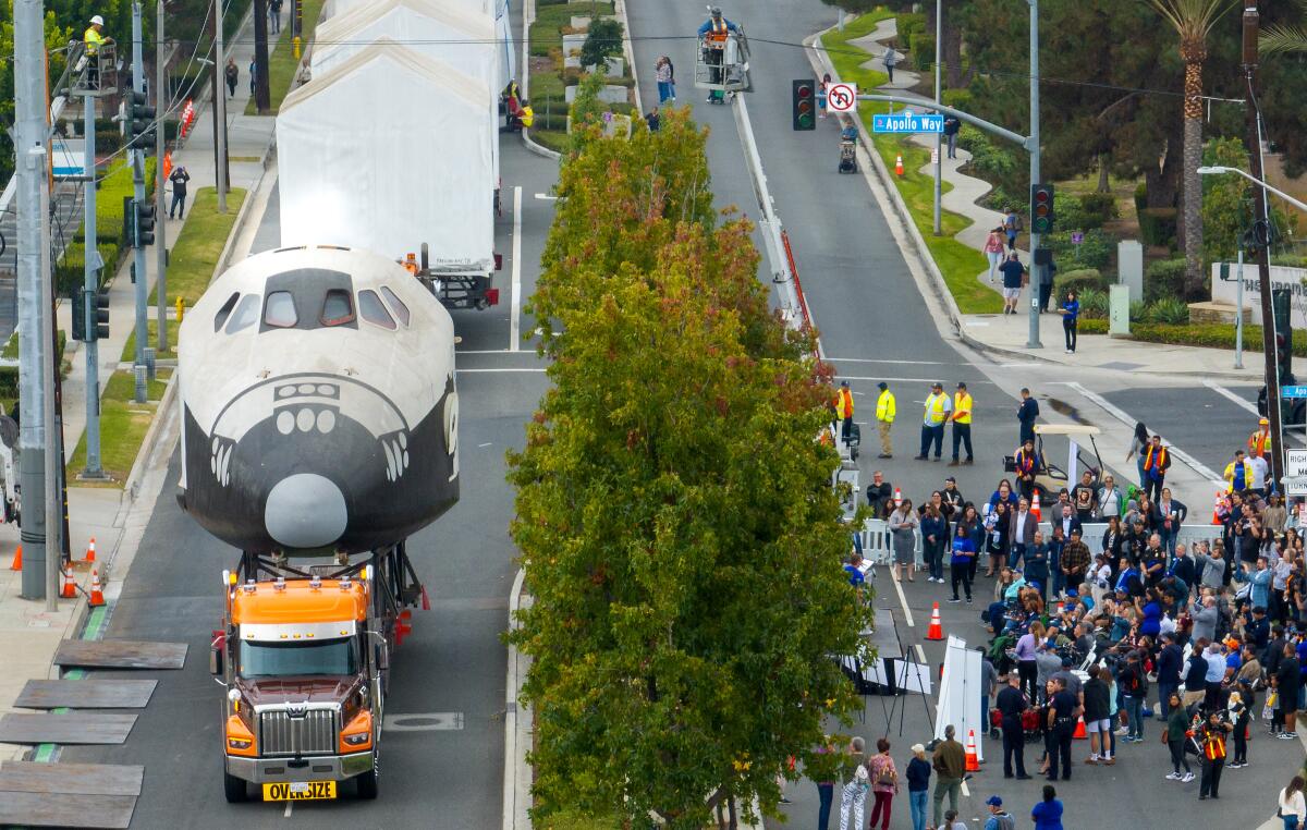 Un modelo a escala de un transbordador espacial se mueve a lo largo de una carretera mientras la gente se reúne para observar.