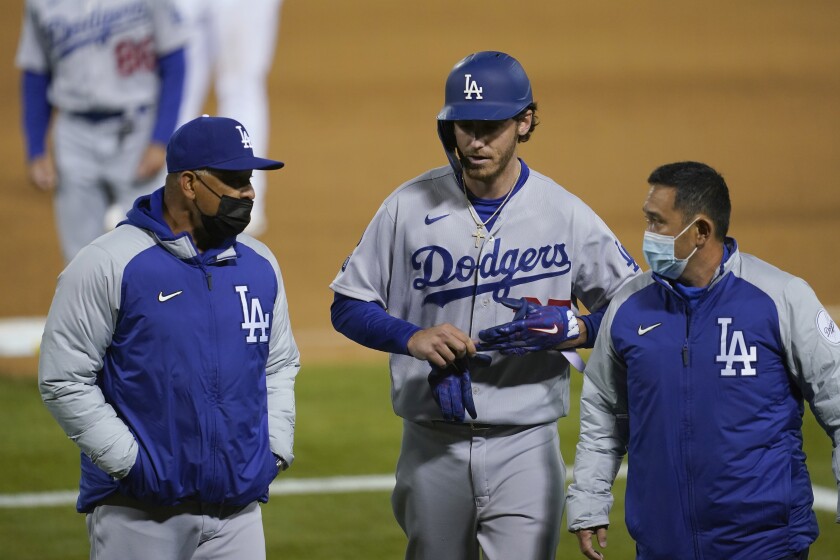 Los Angeles Dodgers' Cody Bellinger, center, walks off the field as he leaves the game with manager Dave Roberts, left, and a trainer during the ninth inning of a baseball game against the Oakland Athletics in Oakland, Calif., Monday, April 5, 2021. (AP Photo/Jeff Chiu)