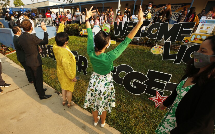 School officials wave to students and parents waiting in line to enter an elementary school.