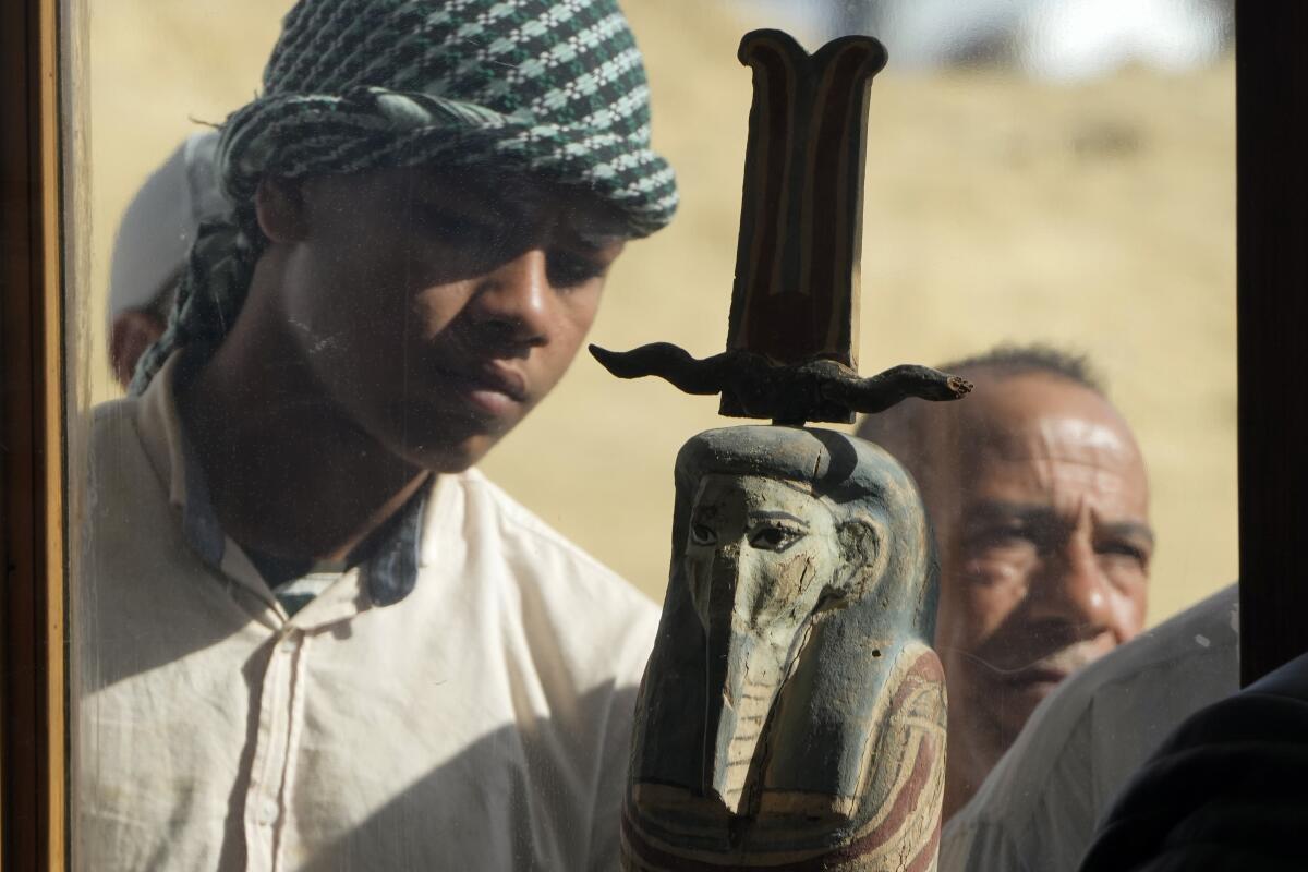 A man with a head covering looks at an artifact resembling an Egyptian mummy with a tall hat