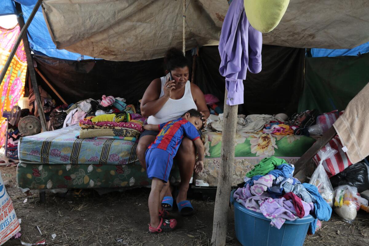 Wendy Guadalupe Contreras, who lost her Honduras home to Hurricane Eta, speaks on the phone while comforting her son.