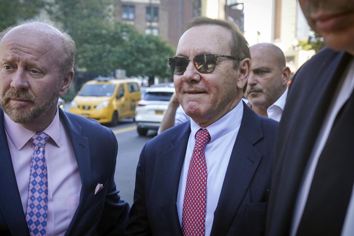 A man in a suit and sunglasses walking on a street with other men in suits