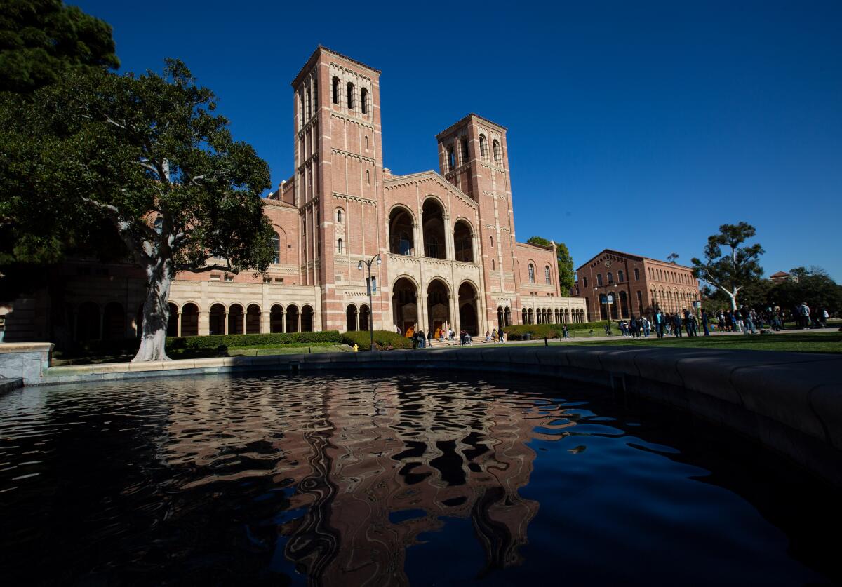 Students walk near Royce Hall at UCLA under blue skies.