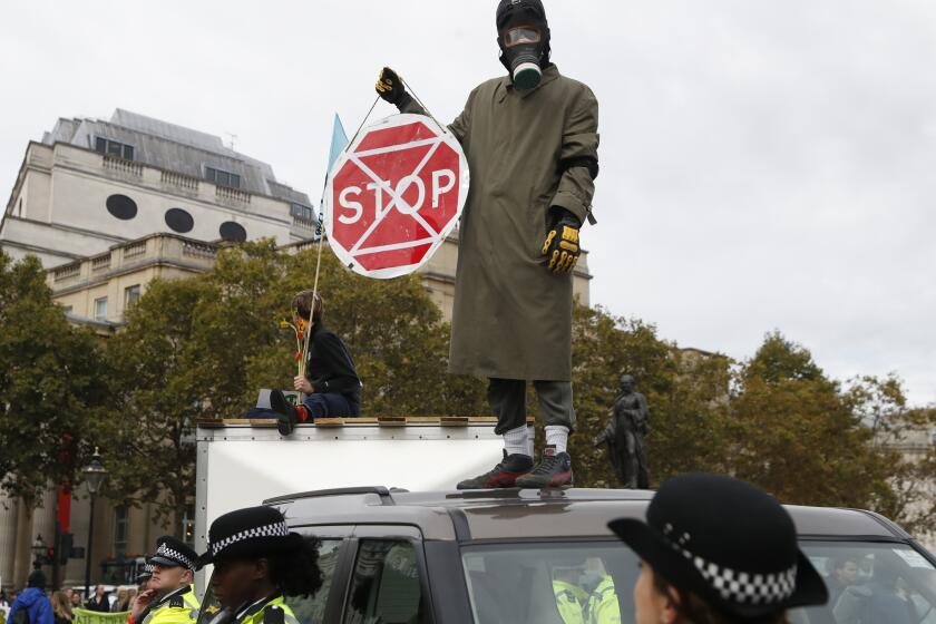 A man wearing a gas mask stand on top of a car as other demonstrators block Trafalgar Square in central London Monday, Oct. 7, 2019. Extinction Rebellion movement blocked major roads in London, Berlin and Amsterdam on Monday at the beginning of what was billed as a wide-ranging series of protests demanding new climate policies. (AP Photo/Alastair Grant)