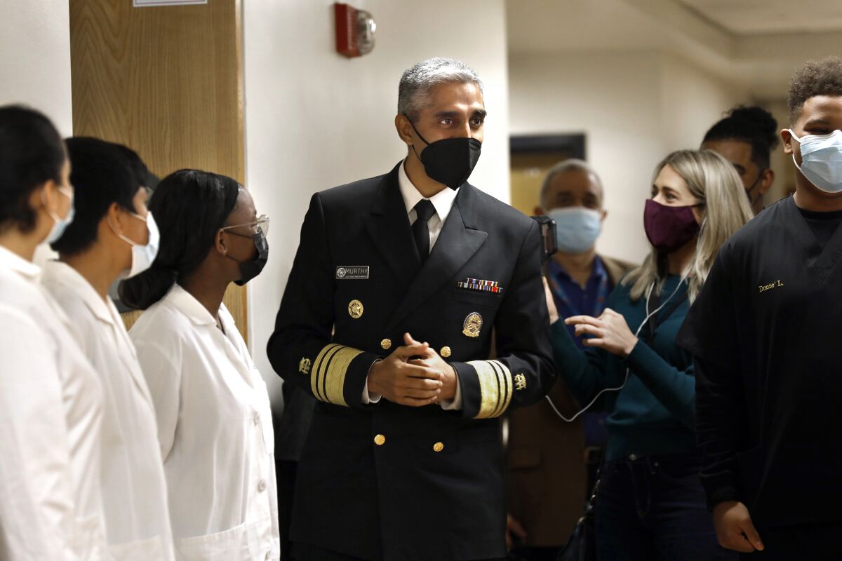 A man in a military uniform and mask walks by people in lab coats and masks.