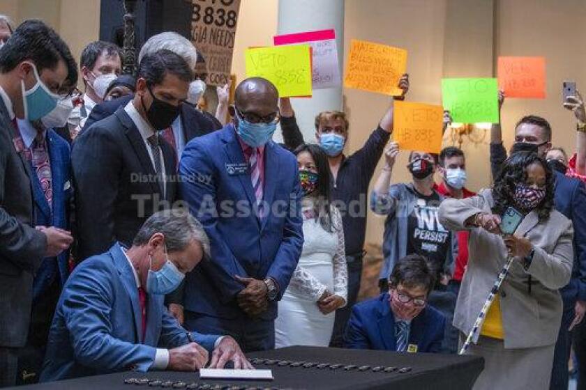 Gov. Brian Kemp, lower left, signs HB 426, hate-crimes legislation, into law as demonstrators hold signs asking him to veto HB 838 in the North Wing of the Georgia State Capitol building Friday, June 26, 2020. Kemp signed into law House Bill 426 which would impose additional penalties for crimes motivated by the victim’s race, color, religion, national origin, sexual orientation, gender or disability. (Alyssa Pointer/Atlanta Journal-Constitution via AP)