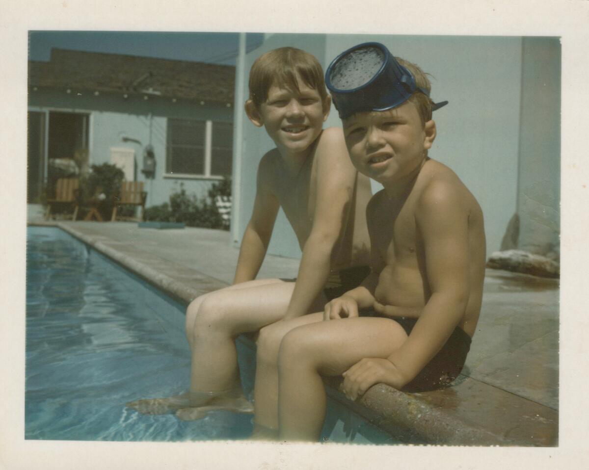 A photo of two young boys in swim trunks, seated with their legs dangling in a swimming pool.
