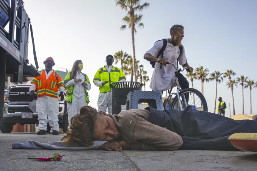 Venice, CA - July 09: A homeless person sleeps on the boardwalk as Los Angeles City cleanup crew gathers to remove homeless encampments on Friday, July 9, 2021 in Venice, CA. (Irfan Khan / Los Angeles Times)
